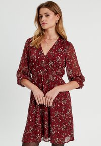 Robe bordeaux à motifs floraux, décolleté en V, taille élastique et manches longues en tulle évasées. Tissu léger avec une ligne d'ourlet fluide.