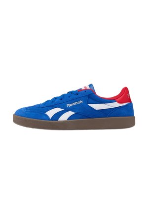 Zapatilla Reebok de ante azul con rayas blancas, cuello del talón rojo, suela marrón y logo de Reebok en el lateral, vista desde el exterior.