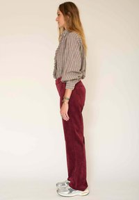 Blouse rayée à volants en gris et blanc, associée à un pantalon en velours côtelé bordeaux. Le modèle porte des baskets argentées et des bijoux simples.