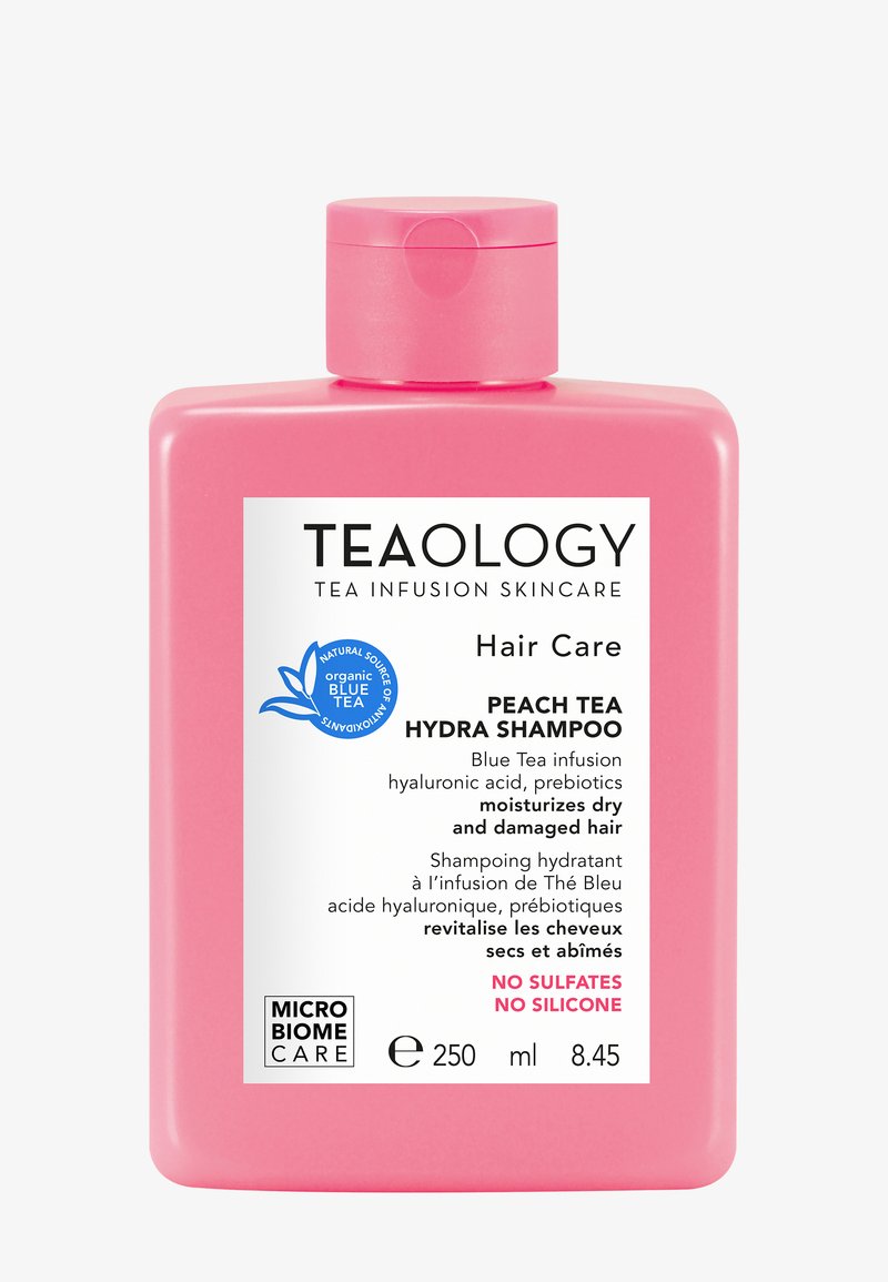 Roze plastic fles perziksenvete Hydra Shampoo, 250 ml. Voorzien van een wit etiket met zwarte tekst en een blauw logo. Geen sulfaten of silicones.