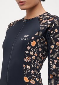 Navy one-piece wetsuit with floral pattern on sleeves, full zipper front, and logo on chest. Made of stretchy material for mobility.