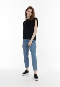 Sort kortærmet top med en tætsiddende pasform, parret med lyseblå jeans med opsmøg. Modellen bærer sorte sneakers med en hvid sål.