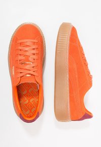 Baskets en suédine orange avec une semelle plateforme texturée marron, dotées de lacets assortis et d'un intérieur orange à motif. Accent de talon bordeaux.
