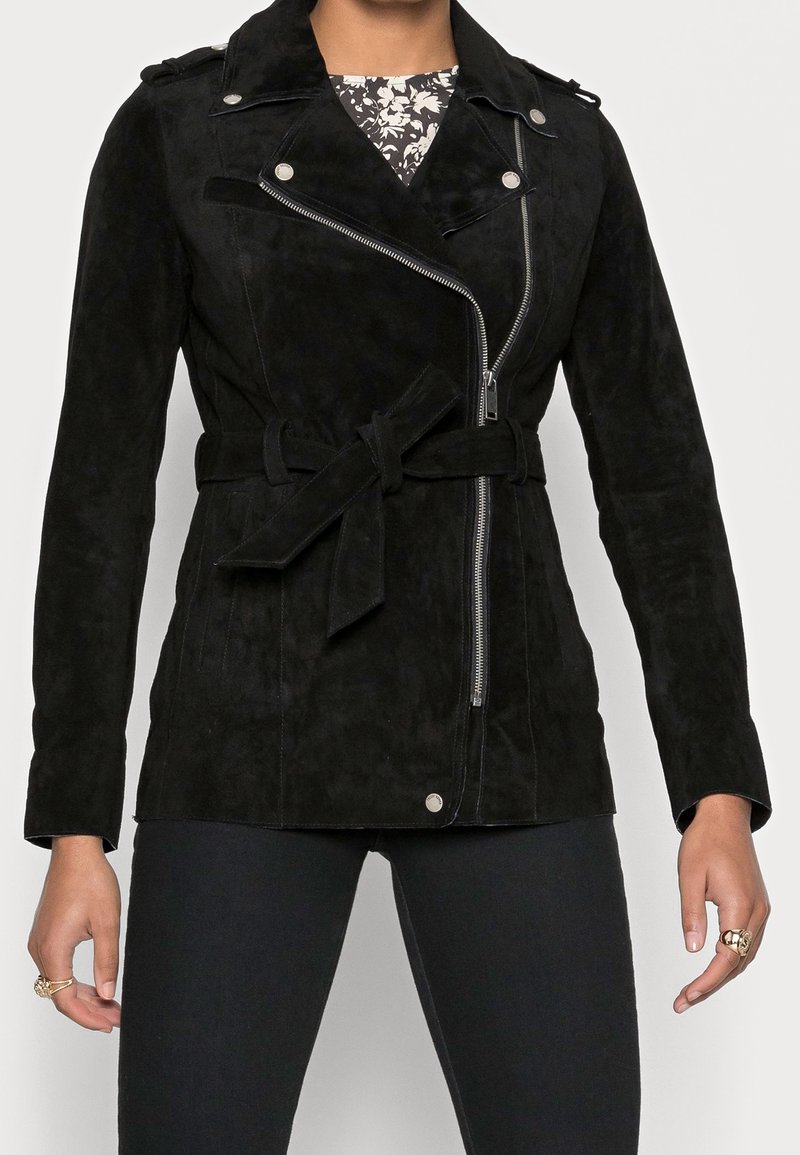 Czarna zamszowa kurtka z zamkiem błyskawicznym z przodu, paskiem w talii i zatrzaskowymi akcentami. Posiada dopasowany krój i naramienniki.