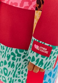 Farebná patchworková bunda s červenými, ružovými a zelenými panelmi s potlačou zvierat. Na rukáve je nálepka s nápisom "Iné farby".