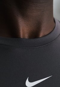 Primo piano del collo di una persona che indossa una maglietta nera Nike con un logo bianco Nike swoosh visibile sul petto.
