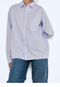 Camicia a maniche lunghe con bottoni di un leggero lavanda, dotata di colletto, con una vestibilità comoda e una texture liscia. Abbinata a jeans in denim blu.