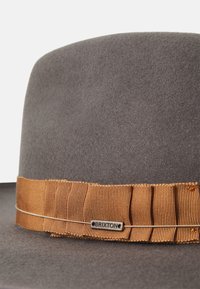 Pălărie gri din fetru, cu o bandă pliată maro ce prezintă eticheta cu logo-ul Brixton. Textura este moale, având un design clasic cu boruri largi.