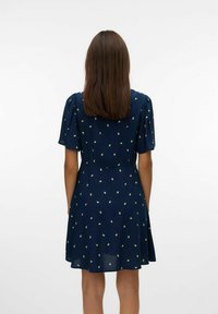 Robe bleu marine à manches courtes avec un ourlet évasé, ornée de pois en forme de feuilles jaune-vert et d'un corsage ajusté. Texture de tissu lisse.