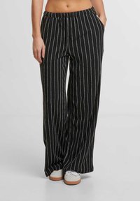 Pánské kalhoty s širokými nohavicemi v černobílém pruhovaném designu a elastickým pasem. Látka má texturovaný povrch. Kombinace s bílými teniskami.