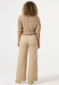 Beiger gestrickter Pullover mit kurzen Puffärmeln, kombiniert mit hochtaillierten beigen weitem Hosen und goldenen Schuhen. Weiche Textur und lässiges Design.