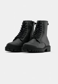 Ghete negre din piele, la gleznă, cu șireturi în față, guler căptușit și talpă din cauciuc masiv cu șanțuri adânci pentru aderență. Detaliu cu fermoar lateral.