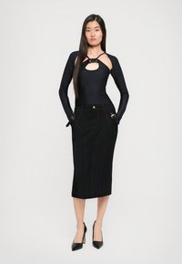 Top preto de manga longa com detalhes recortados na zona do peito, combinado com uma saia midi justa em denim preto com costura de destaque e bolsos frontais.