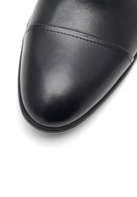 Czarny, wypolerowany skórzany czubek buta z przeszyciem na białym tle.