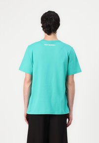 Turquoise cotton t-shirt with short sleeves, crew neck, and a small "marimekko" logo printed at the back near the neckline.
