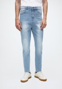 Ljusblå denimjeans med smal passform, med en klassisk femficksdesign och avblekningsdetaljer, kombinerade med vita sneakers.