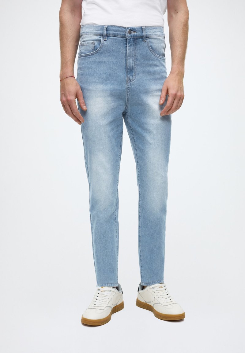 Ljusblå denimjeans med smal passform, med en klassisk femficksdesign och avblekningsdetaljer, kombinerade med vita sneakers.