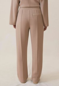 Beige joggingbroek van zacht materiaal, voorzien van een ontspannen pasvorm, geklede naden en een achterzak. Elastiche tailleband voor comfort en gemak.