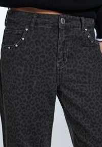 Svarta denimjeans med ett subtilt leopardmönster, silvernitar på fickorna och en klassisk design med fem fickor.