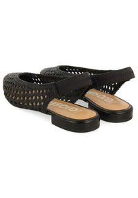 Chaussures slingback tissées noires avec une semelle lisse noire et une semelle intérieure beige, dotées d'une sangle élastique pour un maintien sécurisé.