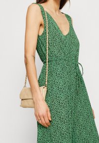 Groene bloemenjurk met een V-hals, gestructureerde stof en een tailleband, gecombineerd met een beige gewatteerde tas met een kettingband.