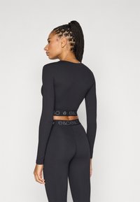 Μαύρο μακρυμάνικο τοπ και ασορτί κολάν από ελαστικό ύφασμα. Το τοπ έχει εφαρμοστή σχεδίαση με λωρίδα με λογότυπο στη μέση.