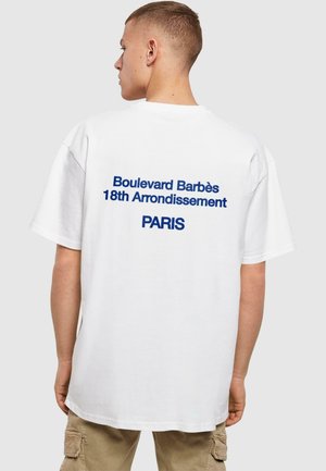 White cotton t-shirt with oversized fit. Back features blue text: "Boulevard Barbès 18th Arrondissement PARIS." Smooth texture.