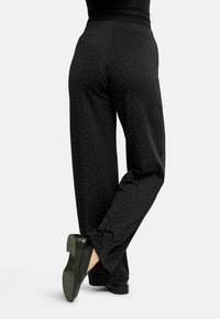 Mustad püksid tikukestemustriga, laiade säärtega, siledast materjalist ja äärtega, kombineeritud mustade jalanõudega.