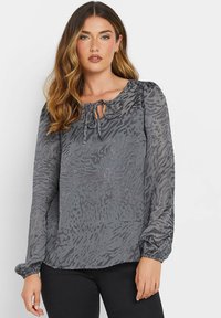 Blusa grigia a maniche lunghe in tessuto leggero con una delicata stampa animale, polsini arricciati e scollatura a chiave con dettaglio a fiocco.