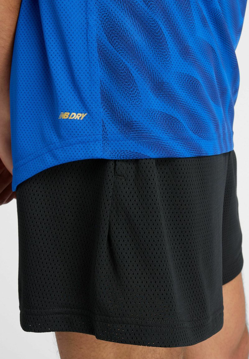 Blauw sportshirt van gaas met een golfpatroon, met zwarte gaasshorts eronder. Gouden "NB DRY" logo aan de zoom van het shirt.