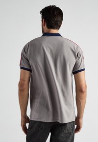 Szary polo z granatowym kołnierzykiem, z czerwonymi paskami na ramionach. Gładka faktura i luźny krój. Brak widocznych kieszeni lub ozdób.