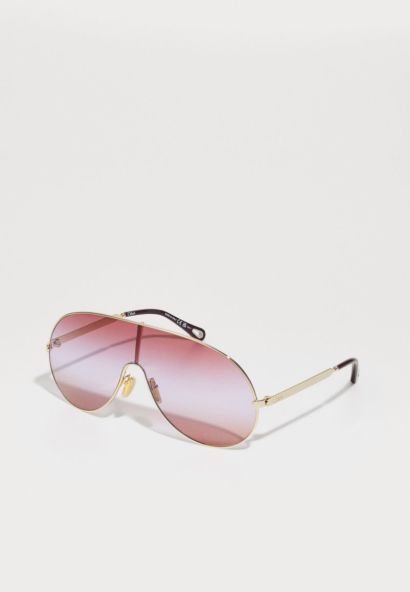 Aviatori stiilis prillid, millel on kuldne metallraam, gradiendi roosad läätsed ja tumedad pruuni atsetaatkõrvapäid. Tuntud kahekordne sild disain.