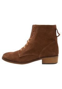 Bottines en suédine marron avec un bout arrondi, un laçage à l'avant, des détails de couture et un petit talon en bois ; comprend une languette à l'arrière.