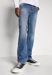 Jeans de mezclilla azul desvaído con corte recto, que presentan un ligero desgastado, diseño de cinco bolsillos y un clásico cierre de botón.