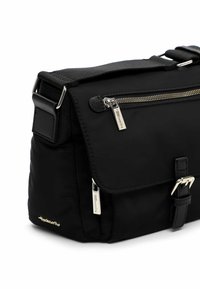 Czarna nylonowa torba na ramię z klapką, przednią kieszenią na zamek, srebrnymi okuciami i regulowanym paskiem, z detalem klamry z przodu.