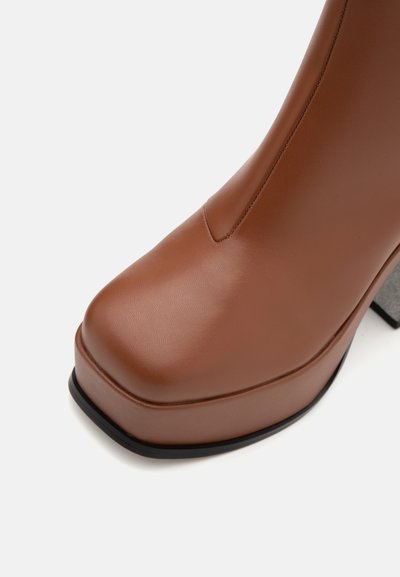 Botte en cuir synthétique marron avec une semelle épaisse et un bout carré, offrant une texture lisse et une semelle noire contrastante.