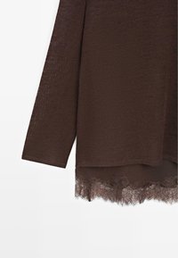 Brown knit top with long sleeves, featuring a lace hem detail at the bottom. The lace is decorative with floral patterns.