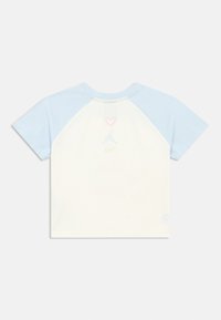 Παιδικό κοντομάνικο μπλουζάκι με ανοιχτόμπλε μανίκια, λευκό σώμα και μικρή ροζ καρδιά, μπλε λογότυπο Nike Air Jordan και πράσινο λογότυπο Nike στη ράχη.