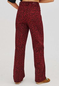 Červené rozšírené nohavice s čiernym leopardím vzorom, s vysokým pásom, zadnými vreckami a textúrovaným povrchom.