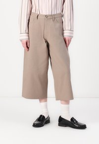 Beige culotter laget av bomull, med rett snitt og lommer, kombinert med svarte loafers og hvite ribbestrikkede sokker. Stripete skjorte er synlig.