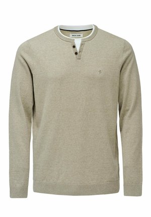 Pull henley beige à manches longues avec trois boutons foncés au niveau du col et un petit logo brodé sur la poitrine.