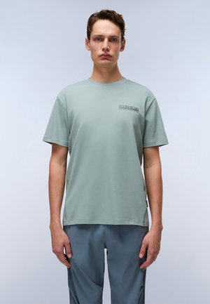 T-shirt vert clair à manches courtes avec un col rond et un petit logo sur la poitrine. Tissu lisse, coupe décontractée, fentes sur les côtés au niveau de l'ourlet.