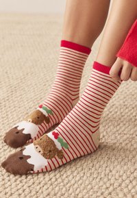 Rot-weiß gestreifte Socken mit illustrierten Bärengesichtern an den Zehen und Stechpalmenakzenten. Gestrickter Stoff, mittlere Wadenlänge.