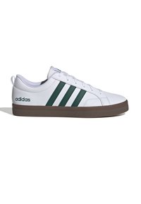 Baskets blanches avec trois bandes vertes, fermeture à lacets, col rembourré et semelle en caoutchouc marron. Présente le logo "adidas" près du talon.