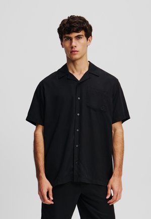 Chemise noire à manches courtes en tissu respirant, avec un devant à boutons, un col pointu et une poche poitrine ornée d'un logo.