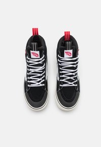 Høye sneakers med svart semsket skinn, hvite lisser, røde detaljer på pull-tab og beige gummisåle. Har logo-patch på tungen.
