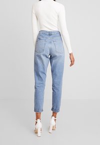 Hochtaillierte hellblaue Jeans mit fünf Taschen, im entspannten Schnitt und umgeschlagenen Säumen, kombiniert mit einem langen weißen Oberteil und weißen Absätzen.