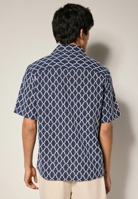 Cămașă cu mânecă scurtă în nuanța bleumarin, cu un model geometric alb. Are guler și o croială lejeră, fiind confecționată dintr-un material ușor.