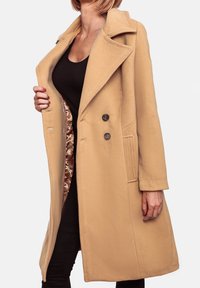 Lange, beige wolmix jas met een geknikte kraag, twee grote voorknopen en zijzakken. Satijnen voering met een subtiel patroon dat zichtbaar is.