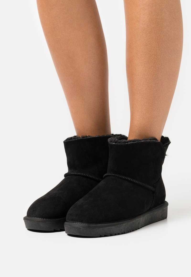 Černé semišové kotníkové boty s měkkou umělou kožešinou uvnitř, zaoblenou špičkou a strukturovanou gumovou podrážkou. Skládaný detail na vrchu.